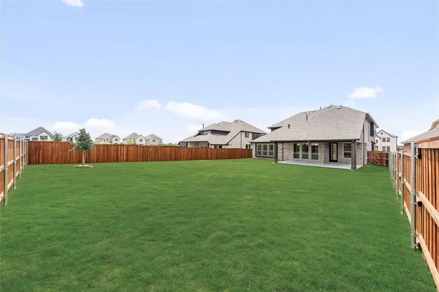 Large backyard with green lawn, wood privacy fence, and covered patio on brick home