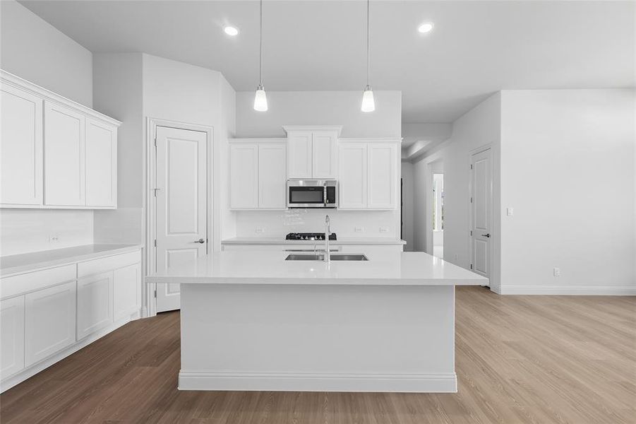 Kitchen featuring white cabinetry, dark wood-style floors, a center island with sink, hanging light fixtures, and light stone countertops