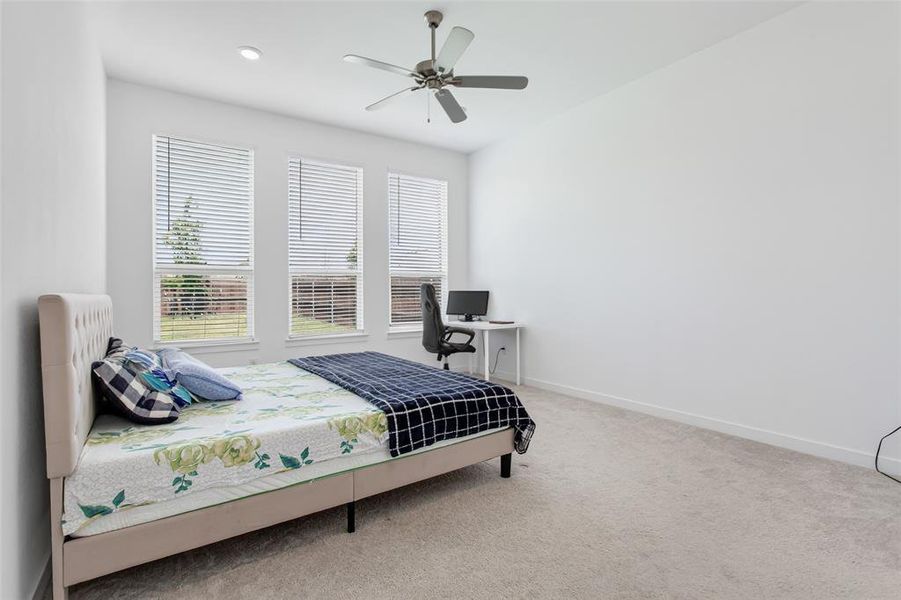 Spacious room with light-colored carpeting, three windows with horizontal blinds, and a ceiling fan