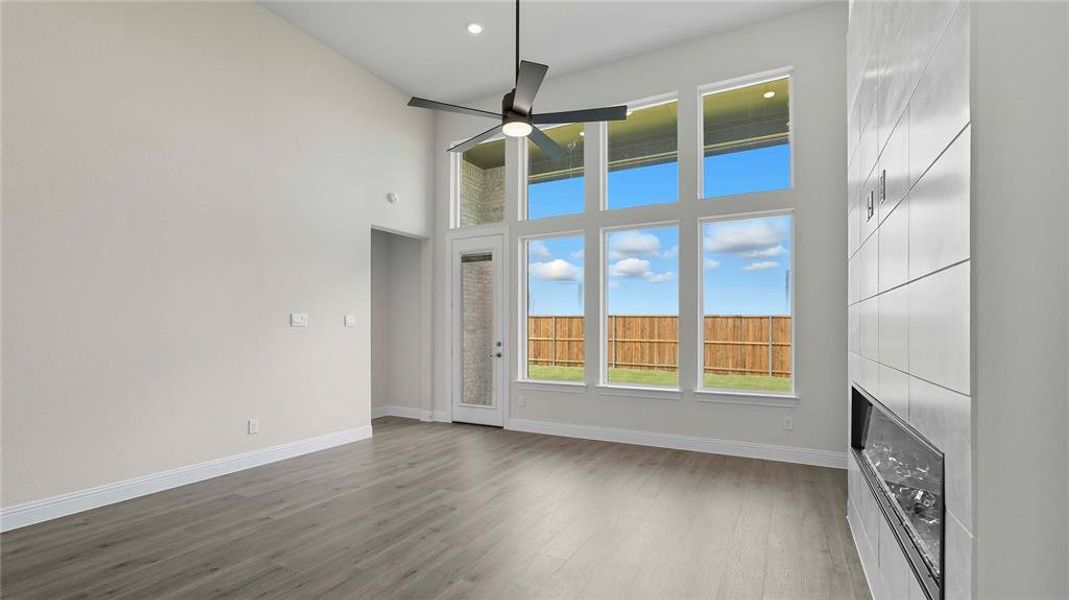 Vaulted ceiling living area featuring wood-finish flooring, a contemporary ceiling fan, and a built-in fireplace with a tiled surround