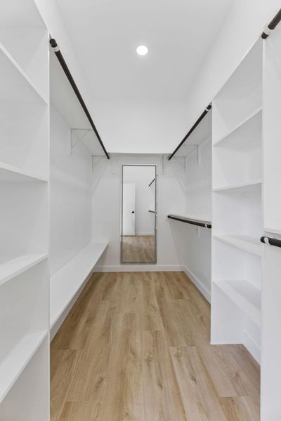A spacious walk-in closet includes extensive built-in shelving and light wood flooring.