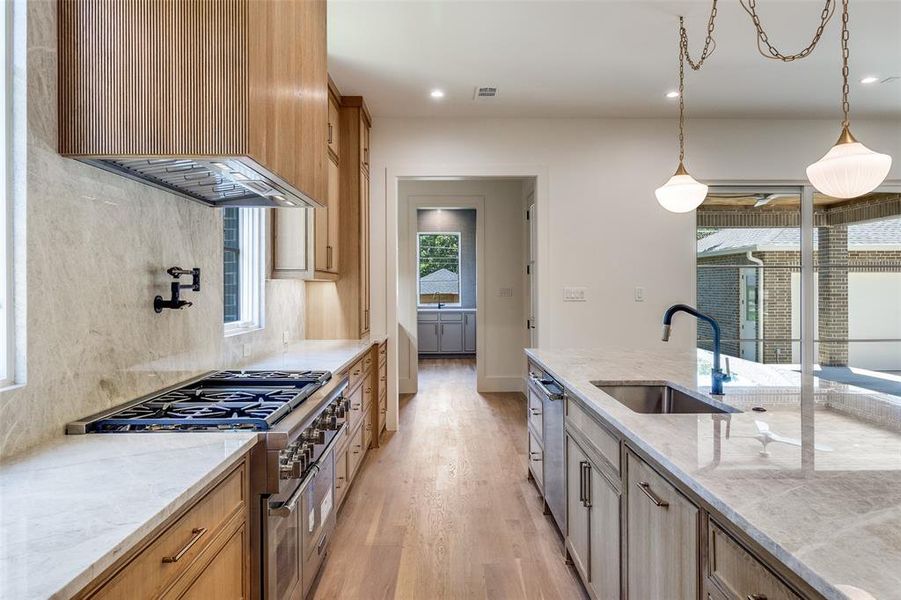 Kitchen with light stone countertops, light wood-style flooring, stainless steel stove, pendant lighting, and recessed lighting Kitchen with light stone countertops, light wood-style flooring, stainless steel stove, pendant lighting, and recessed lighting