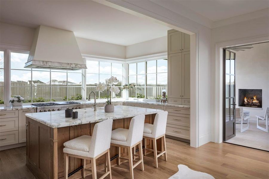 Kitchen with light stone counters, light wood-style floors, premium range hood, a breakfast bar, and a center island with sink Kitchen with light stone counters, light wood-style floors, premium range hood, a breakfast bar, and a center island with sink