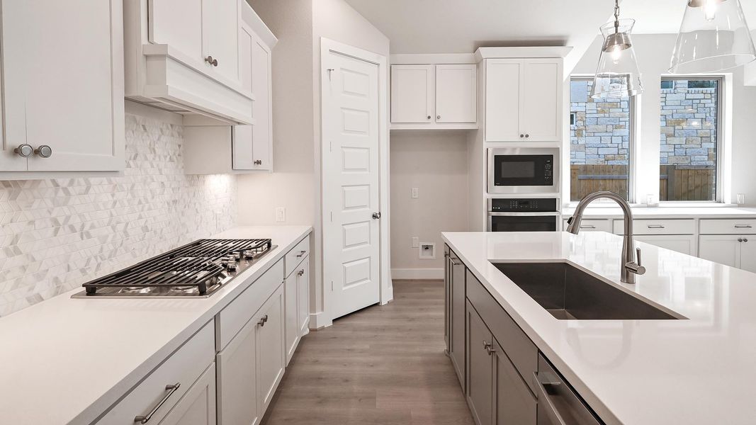 Kitchen featuring wood finished floors, stainless steel appliances, white cabinetry, backsplash, and decorative light fixtures Kitchen featuring wood finished floors, stainless steel appliances, white cabinetry, backsplash, and decorative light fixtures