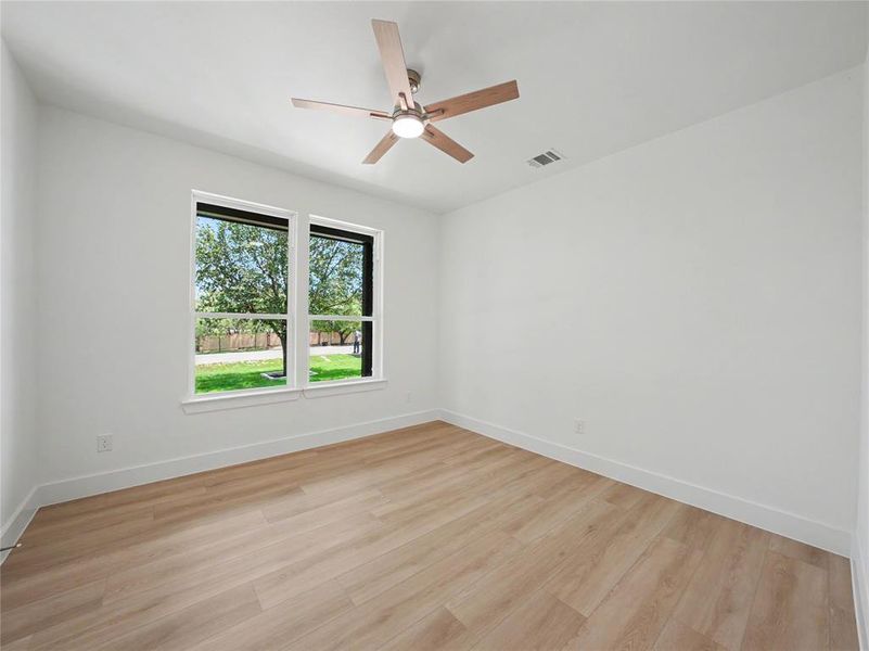 Spacious room featuring wood-finish flooring, crisp white walls, and a contemporary ceiling fan Spacious room featuring wood-finish flooring, crisp white walls, and a contemporary ceiling fan