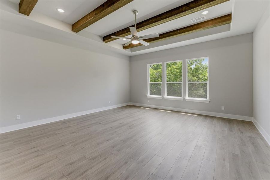Recessed tray ceiling with exposed wood beams, wood-finish flooring, and a ceiling fan