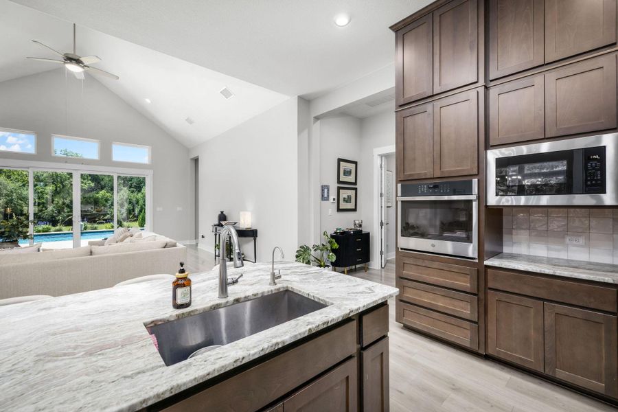 A well-appointed kitchen island with a stainless steel sink connects to a sun-drenched living area with vaulted ceilings.