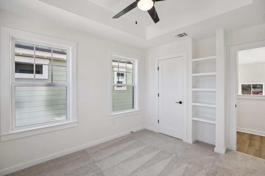 Unfurnished bedroom featuring light colored carpet, a tray ceiling, and a ceiling fan