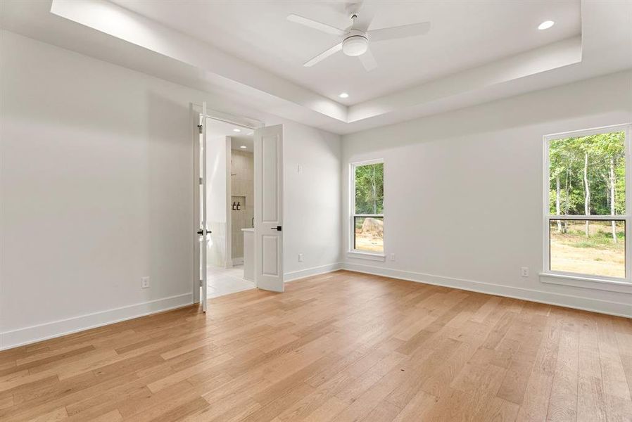 Empty room featuring a raised ceiling, light wood-type flooring, recessed lighting, and a ceiling fan