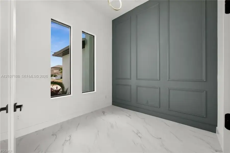 Interior space featuring large-format tile flooring with a neutral veining pattern, charcoal-toned wall with wainscoting molding, dual tall windows, and matte black hardware