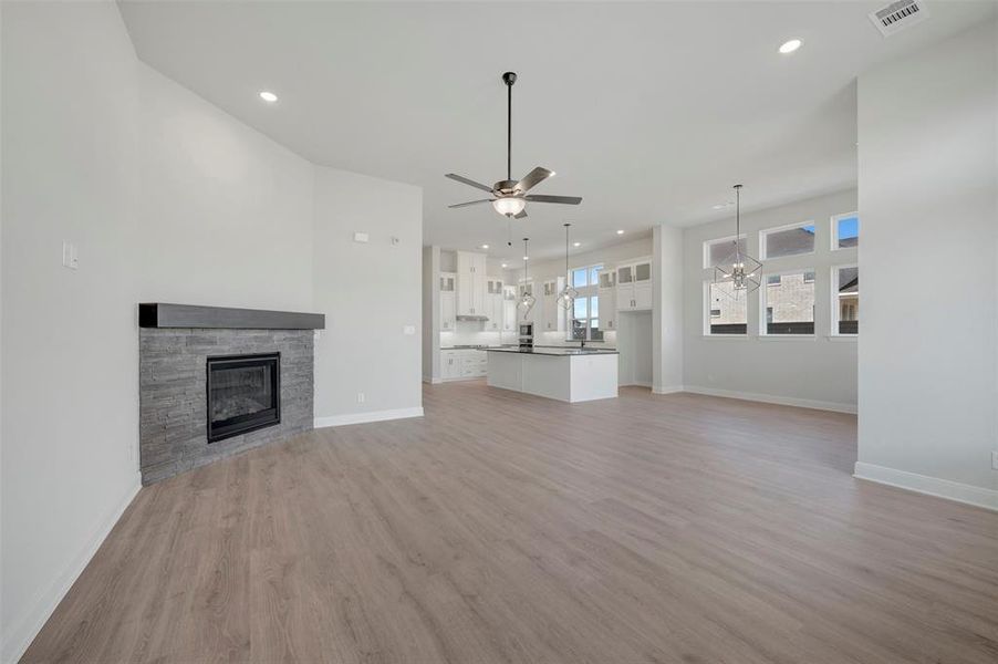 Unfurnished living room featuring a stone fireplace, light wood-style flooring, a ceiling fan, and recessed lighting