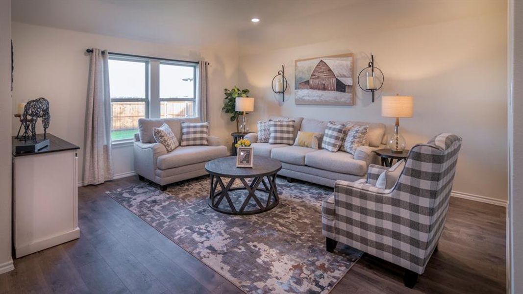 Spacious living area featuring light-toned walls, wood-finish flooring, and a large window offering natural light
