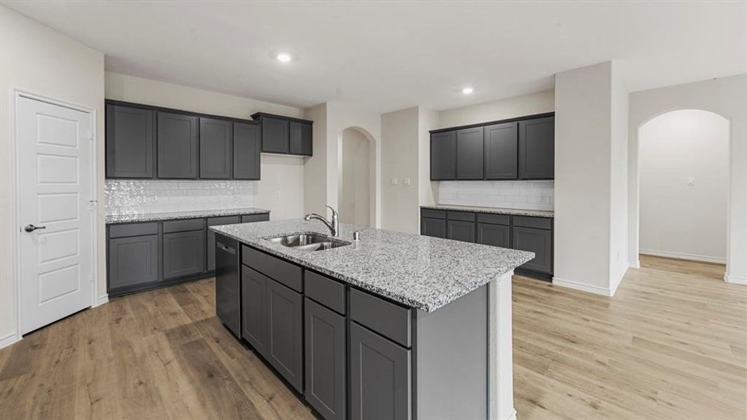 Kitchen featuring a central island with an undermount sink, granite countertops, and dark gray cabinetry