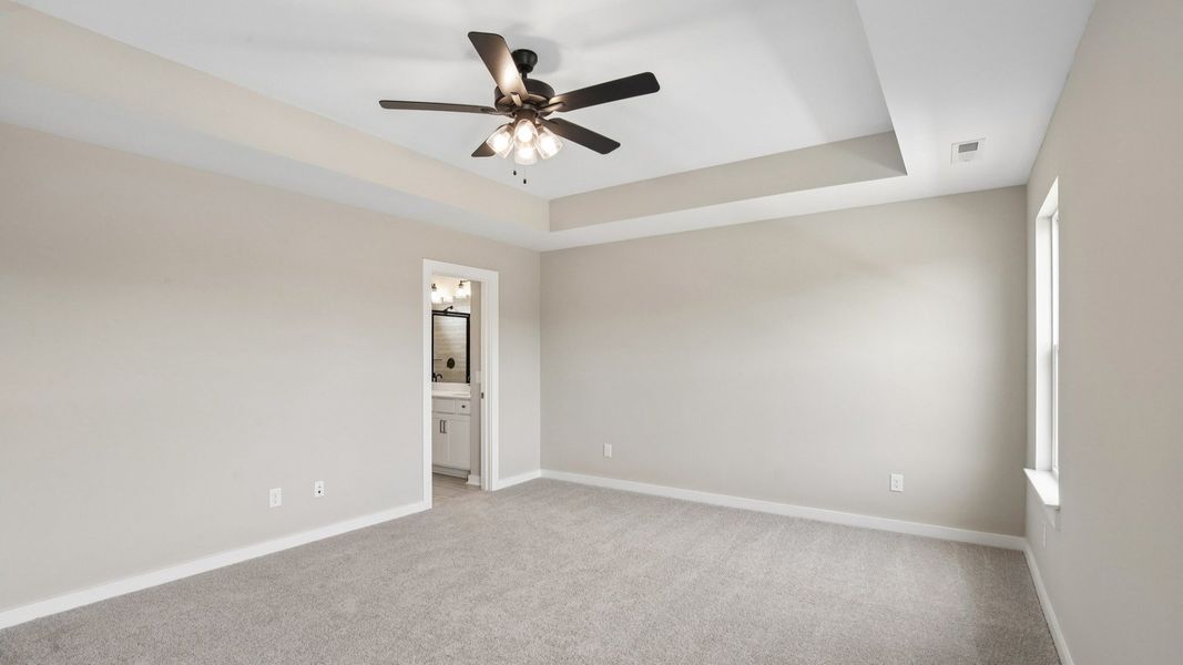 Bedroom with tray ceiling, windows, and entrance to primary bathroom Bedroom with tray ceiling, windows, and entrance to primary bathroom