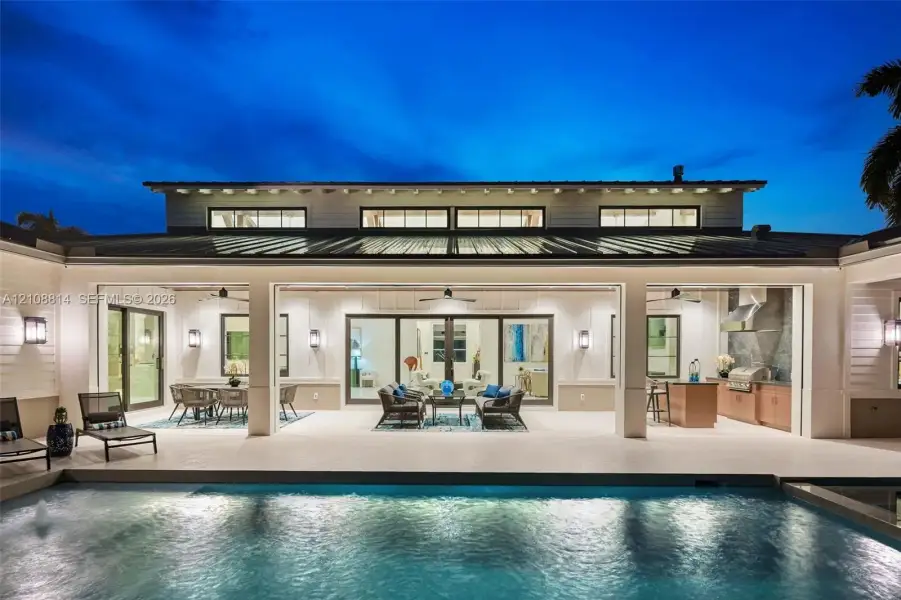 Covered outdoor living area featuring a metal roof, expansive glass door openings, built-in outdoor kitchen with cabinetry, integrated ceiling fans, and a private swimming pool Covered outdoor living area featuring a metal roof, expansive glass door openings, built-in outdoor kitchen with cabinetry, integrated ceiling fans, and a private swimming pool
