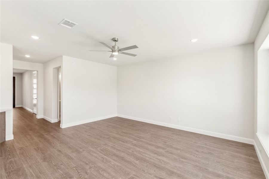 Empty living room with wood-look floors, ceiling fan, white walls, and recessed lighting