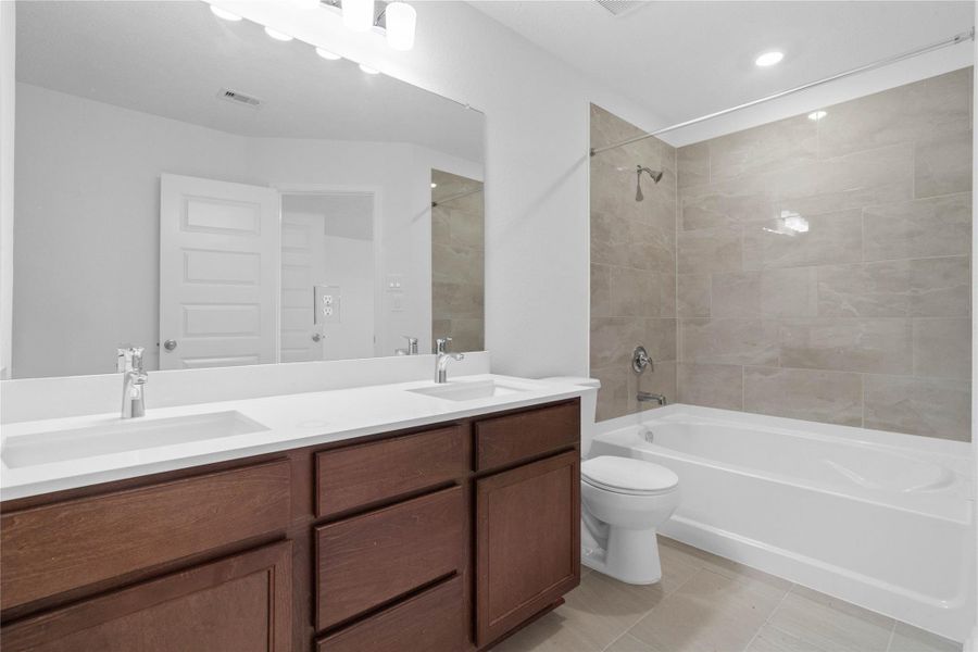 The primary bathroom offers a spacious tub/shower combination with a tiled surround, stained cabinetry topped with light countertops, dual sinks, high ceilings, neutral paint, a large mirror, and sleek, modern finishes for a polished look. The primary bathroom offers a spacious tub/shower combination with a tiled surround, stained cabinetry topped with light countertops, dual sinks, high ceilings, neutral paint, a large mirror, and sleek, modern finishes for a polished look.