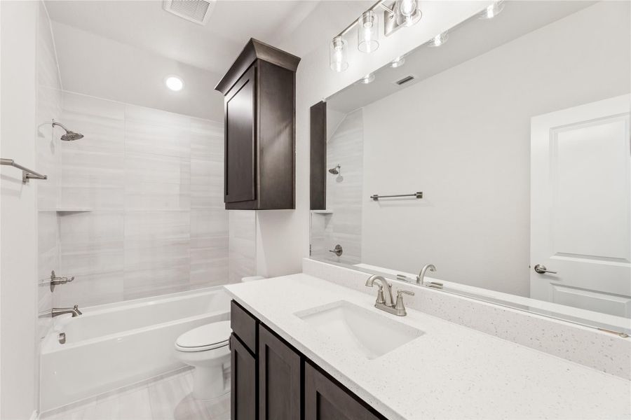 Bathroom with dark wood vanity, white quartz countertop, tub-shower combo, and tiled walls Bathroom with dark wood vanity, white quartz countertop, tub-shower combo, and tiled walls