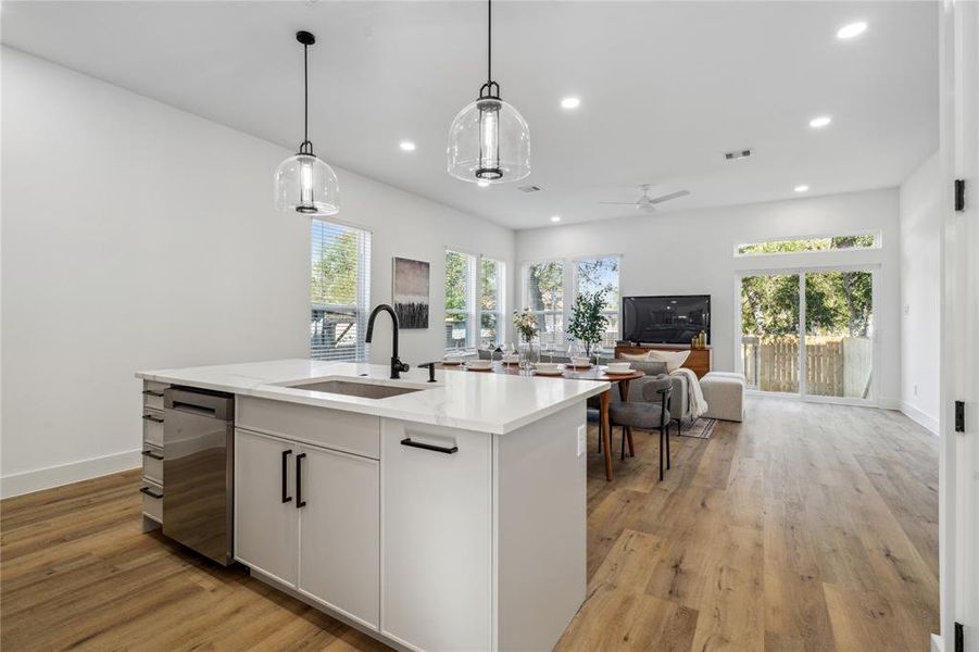 Bright and open concept living area with a stunning kitchen island at the heart, large windows for ample natural light, and seamless indoor-outdoor access through sliding glass doors to the backyard.