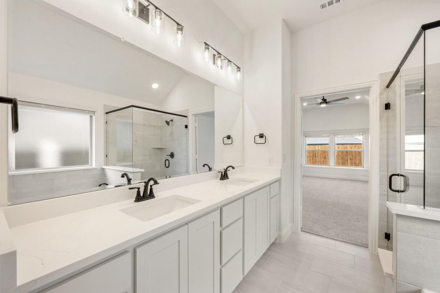 Master bathroom with double vanity, white cabinets, large mirror, and glass shower enclosure Master bathroom with double vanity, white cabinets, large mirror, and glass shower enclosure