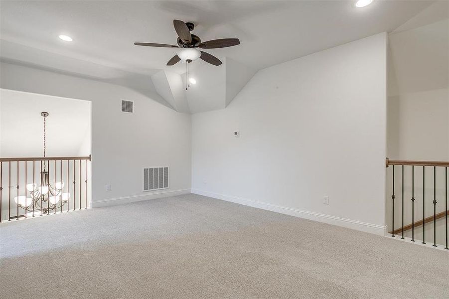 Carpeted empty room with lofted ceiling and ceiling fan with notable chandelier