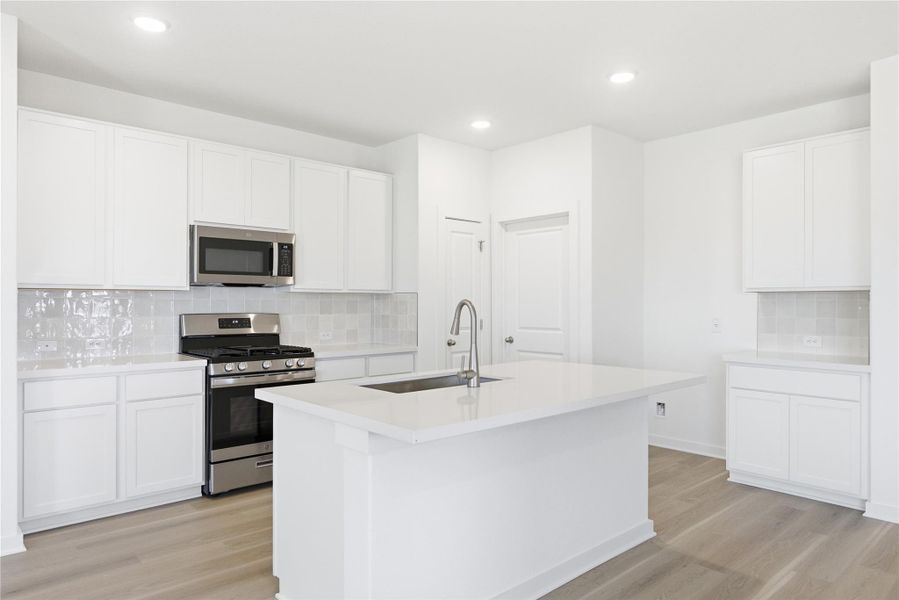Kitchen featuring tasteful backsplash, stainless steel appliances, light wood-style flooring, white cabinets, and an island with sink
