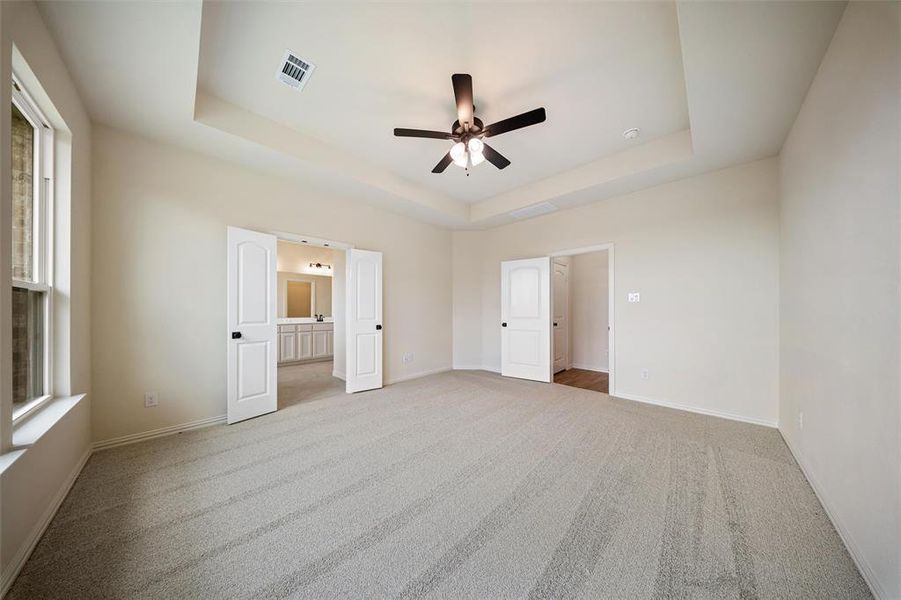 Unfurnished bedroom featuring a tray ceiling, carpet flooring, multiple windows, and ensuite bath