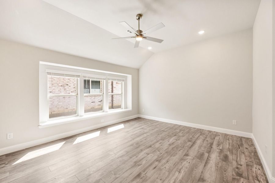 Empty room with vaulted ceiling, ceiling fan, hardwood floors, and large triple window