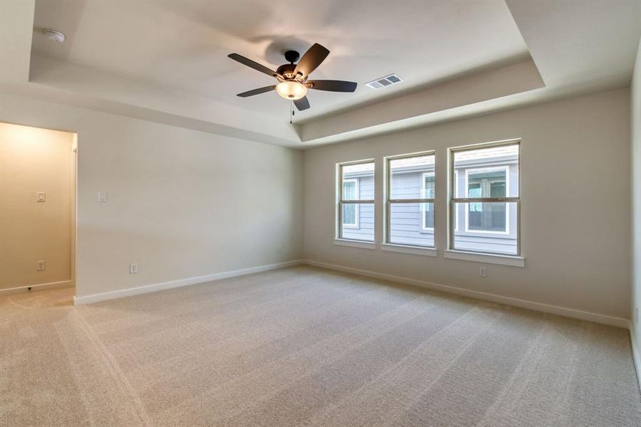 Unfurnished room featuring a tray ceiling, light colored carpet, and ceiling fan Unfurnished room featuring a tray ceiling, light colored carpet, and ceiling fan