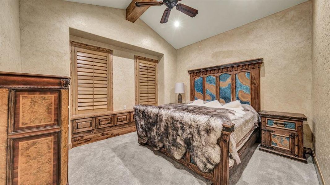Guest bedroom with vaulted ceiling, wood beam accents, and natural light through wood-framed windows.