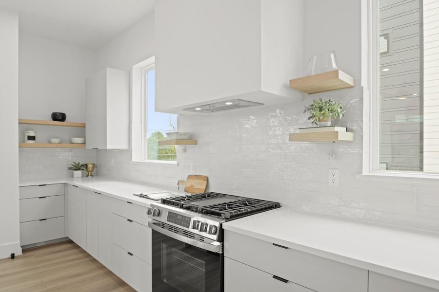 Fixed windows flank the range and sit above the quartz counters adding natural light which illuminates the abundance of counter space on each side along with floating shelves. Fixed windows flank the range and sit above the quartz counters adding natural light which illuminates the abundance of counter space on each side along with floating shelves.