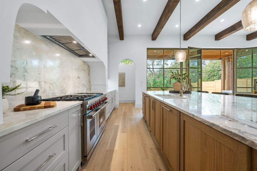 Kitchen featuring light stone countertops, decorative light fixtures, brown cabinetry, range with two ovens, and light wood finished floors Kitchen featuring light stone countertops, decorative light fixtures, brown cabinetry, range with two ovens, and light wood finished floors