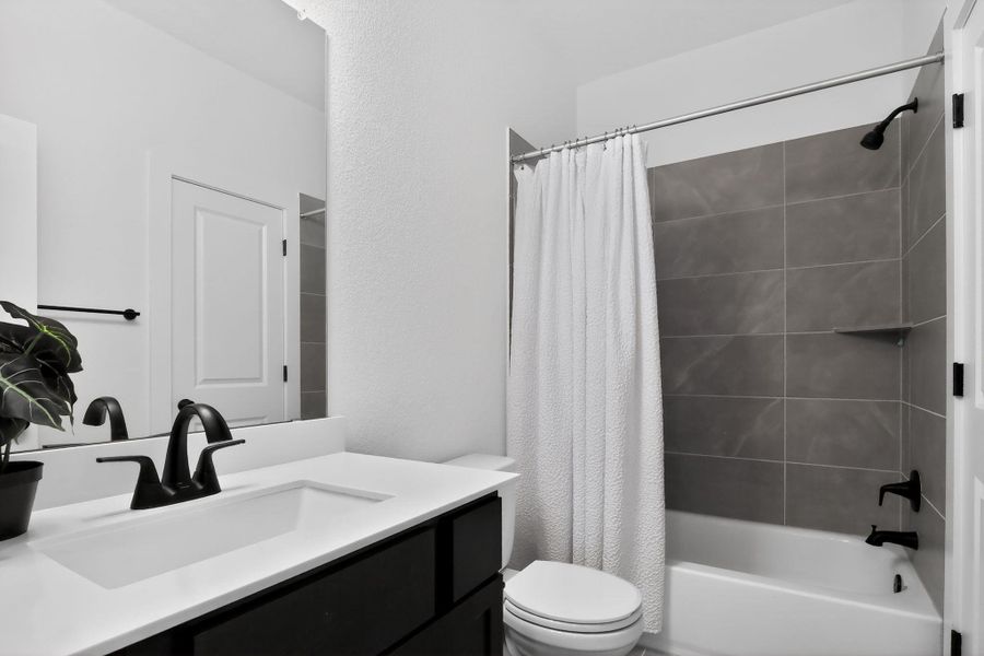 Bathroom featuring a white bathtub and shower with gray tile surround, matte black shower fixtures, and a corner shelf Bathroom featuring a white bathtub and shower with gray tile surround, matte black shower fixtures, and a corner shelf