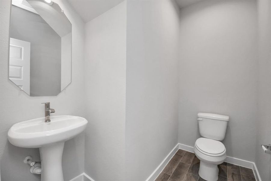 This half bathroom features a stylish pedestal sink, modern hardware, and bright recessed lighting, creating a sleek and inviting space. Sample photo of completed home with similar floor plan. Actual colors and selections may vary.