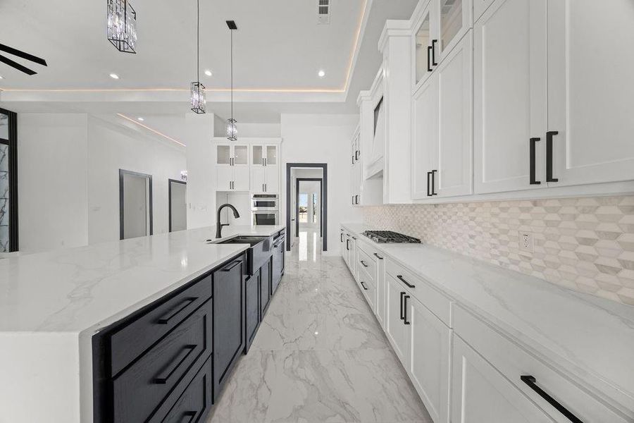 Kitchen with glass insert cabinets, light stone countertops, dual tone cabinets, and decorative light fixtures