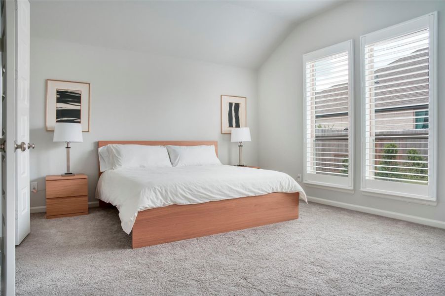 This bedroom features a spacious layout with a large bed, neutral carpeting, and ample natural light from tall windows with blinds. Simple decor and matching wooden nightstands create a modern, cozy atmosphere. This bedroom features a spacious layout with a large bed, neutral carpeting, and ample natural light from tall windows with blinds. Simple decor and matching wooden nightstands create a modern, cozy atmosphere.