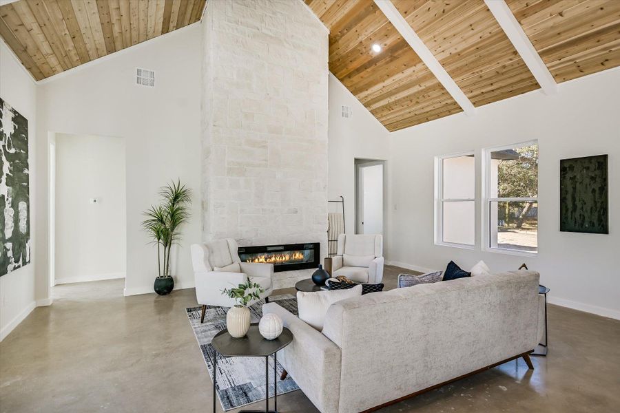 Living room featuring finished concrete floors, high vaulted ceiling, a stone fireplace, and wood ceiling