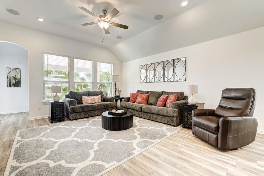 Living area with wood finished floors, a ceiling fan, lofted ceiling, arched walkways, and recessed lighting