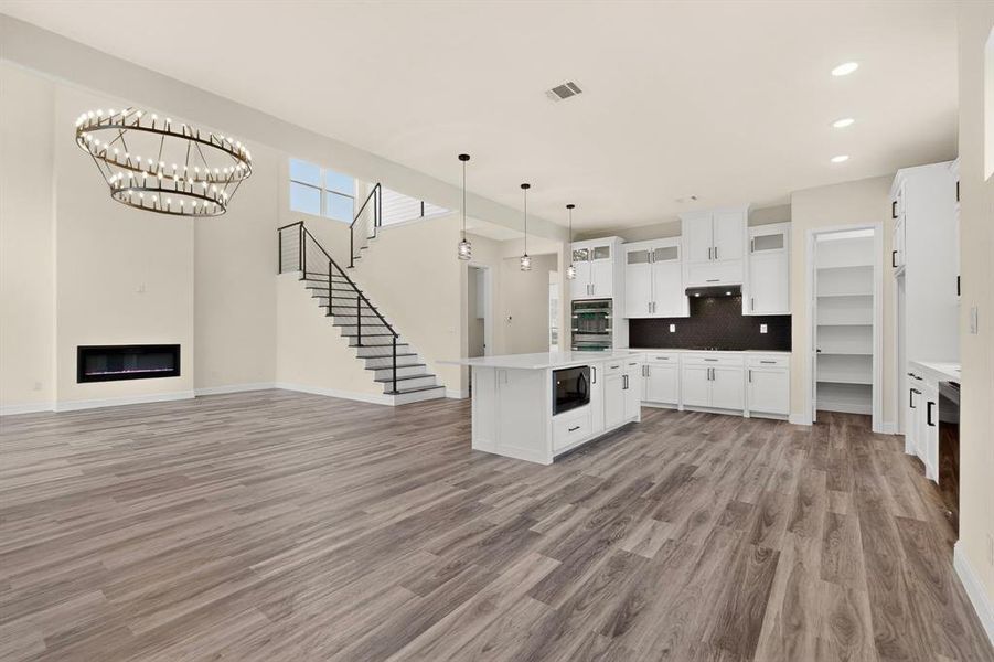 Open-concept living space featuring wood-finish flooring, a contemporary linear fireplace, and a striking tiered chandelier