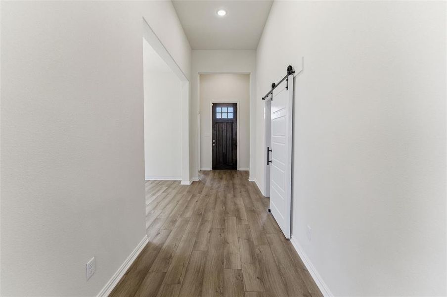 Corridor featuring a barn door, light wood finished floors, and recessed lighting