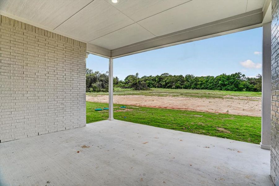 Spacious covered patio with light-colored brick wall, concrete flooring, and recessed ceiling lighting