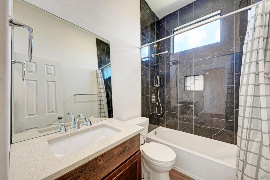 Dark marble-patterned tile surrounds the tub shower alongside a rustic wood vanity with stone counters.