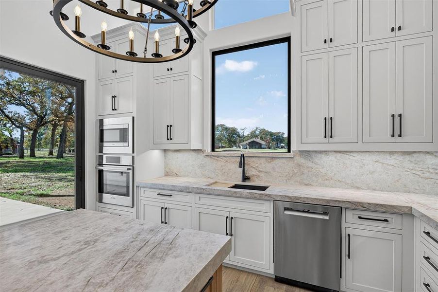 Kitchen featuring appliances with stainless steel finishes, a chandelier, light stone counters, and plenty of natural light