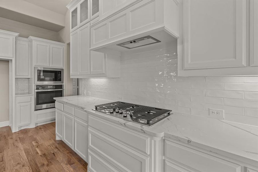 Kitchen featuring light stone counters, stainless steel appliances, custom exhaust hood, and white cabinets