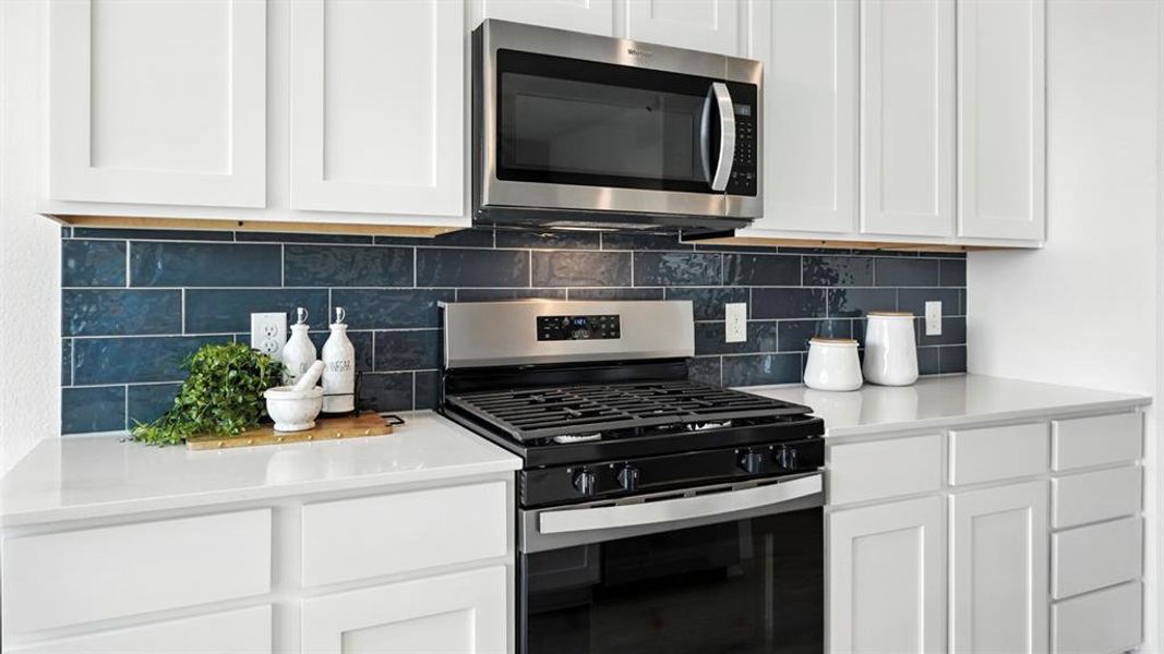 White shaker-style cabinetry with a dark blue subway tile backsplash and stainless steel appliances, including a gas range and microwave