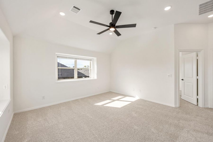 Empty bedroom with white walls, beige carpet, vaulted ceiling, and black ceiling fan