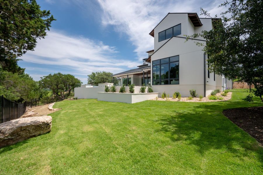 A lush green lawn wraps around the modern residence, with ample space for outdoor enjoyment.