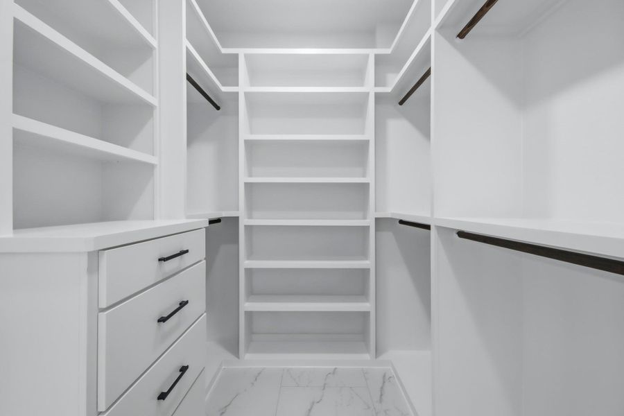 This massive primary walk-in closet features extensive custom floor-to-ceiling shelving, multiple hanging rods with dark accents, a built-in dresser with matte black hardware. This massive primary walk-in closet features extensive custom floor-to-ceiling shelving, multiple hanging rods with dark accents, a built-in dresser with matte black hardware.