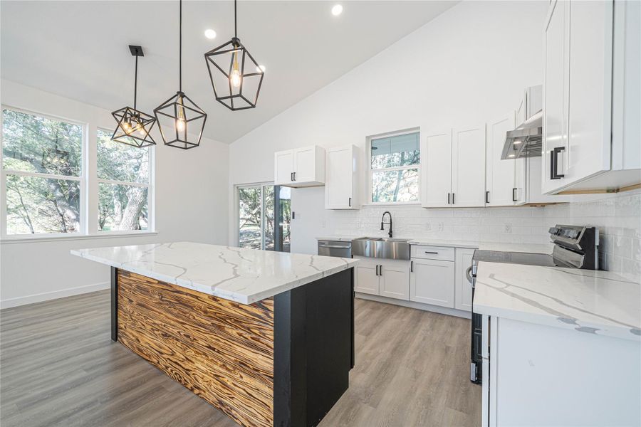 Kitchen with a kitchen island, light stone counters, electric stove, white cabinets, and high vaulted ceiling