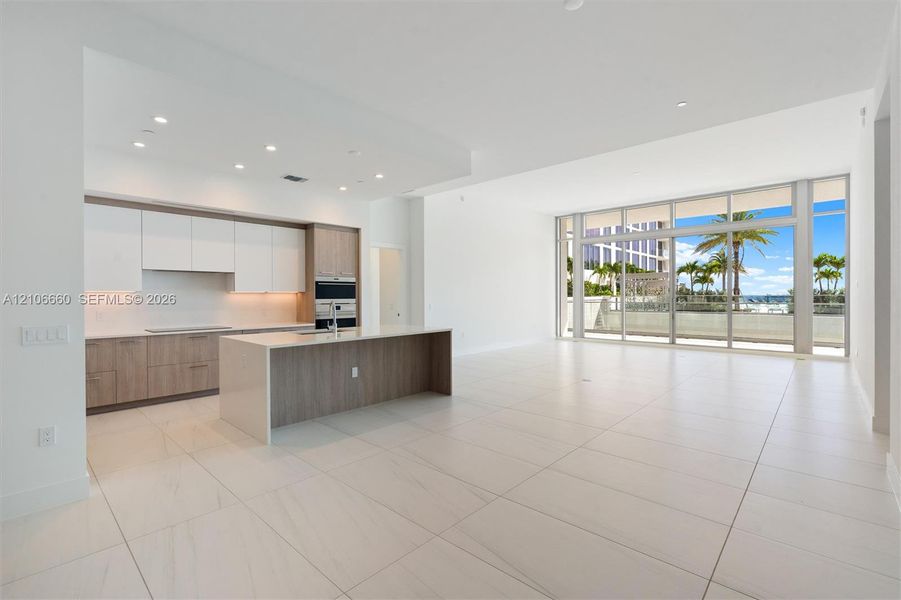 Open-concept kitchen featuring two-toned cabinetry, a stone-surface island, built-in double ovens, recessed lighting, and expansive floor-to-ceiling glass doors